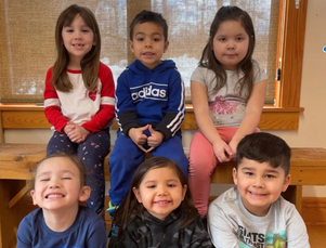Six smiling children in two rows of three in front of a window with snow outside.